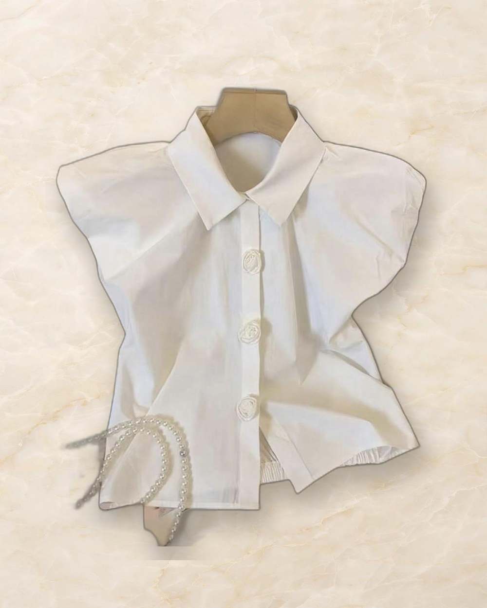 Camisa blanca de botones con botones en forma de rosa., aislado sobre mármol marfil