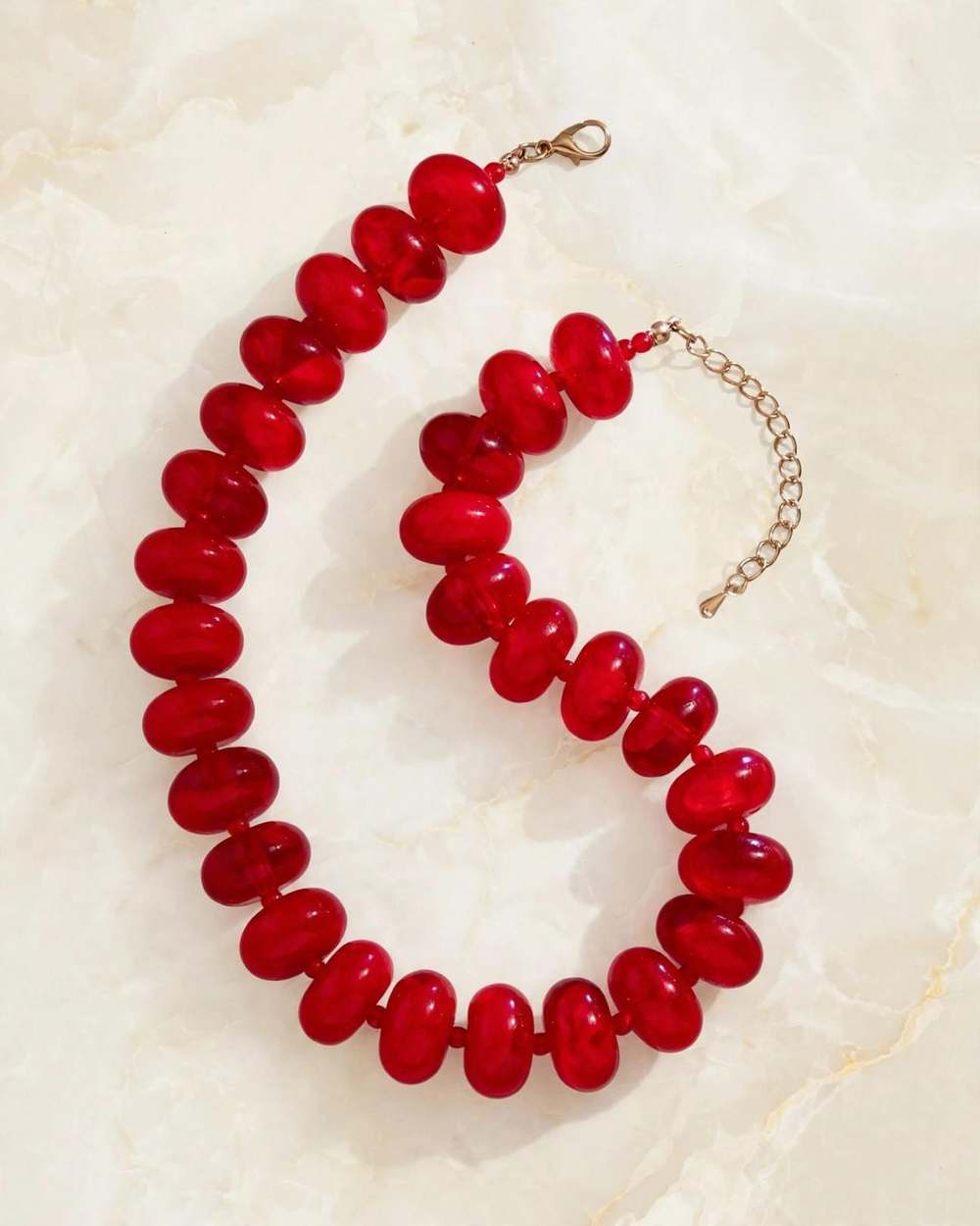 Collar de perlas rojas con broche y cadena dorada, aislado sobre mármol marfil
