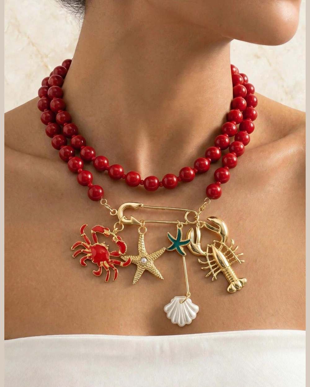 Modelo con collar rojo de perlas y portadijes dorado con charms marinos (cangrejo, estrella, langosta, caracola)