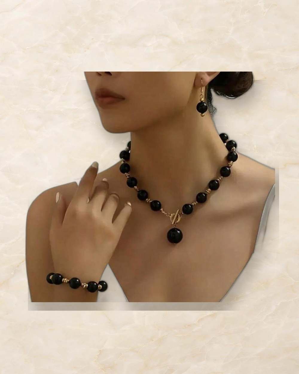 Set de collar de perlas negras con separadores dorados, dije colgante, zarcillos y pulsera a juego., aislado sobre mármol marfil