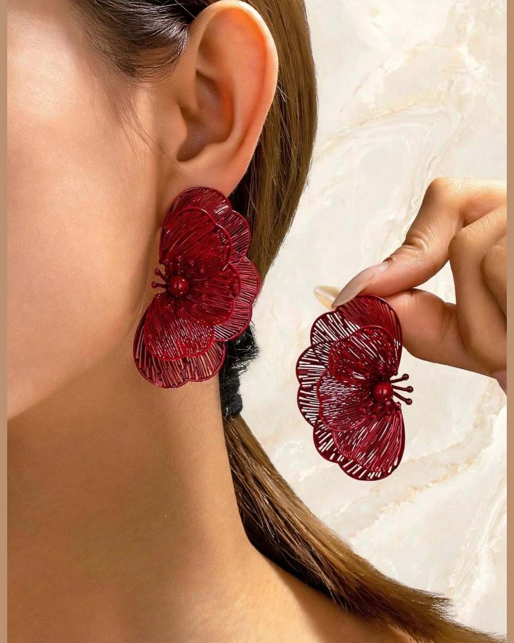 Modelo con zarcillos de flor roja (uno puesto, otro en mano)