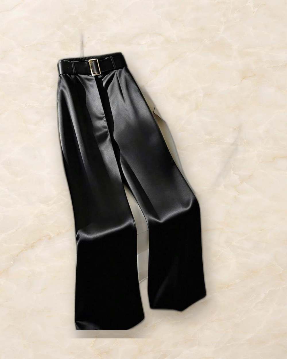 Pantalon negro satinado de pierna ancha con cinturon., aislado sobre mármol marfil